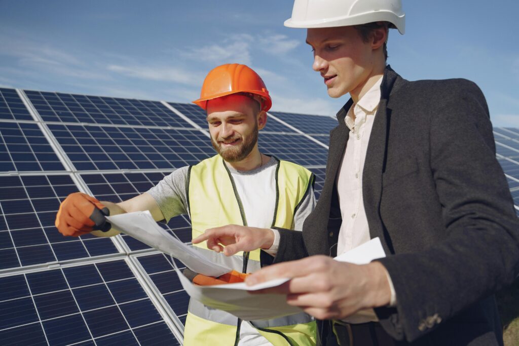 pexels photo 4254157 4254157 Low angle of young engineer and businessman in hardhats discussing project details against solar energy station