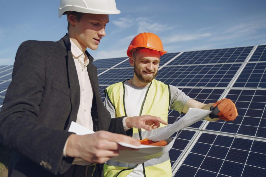 pexels photo 4254157 4254157 Low angle of young engineer and businessman in hardhats discussing project details against solar energy station